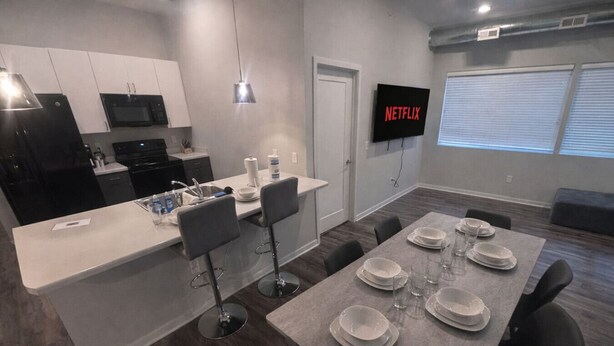 A modern kitchen with a dining area, a flat-screen TV, and a large window.