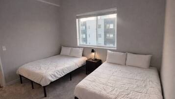 A room with two single beds, a small table with a lamp, and a window with a view of buildings.