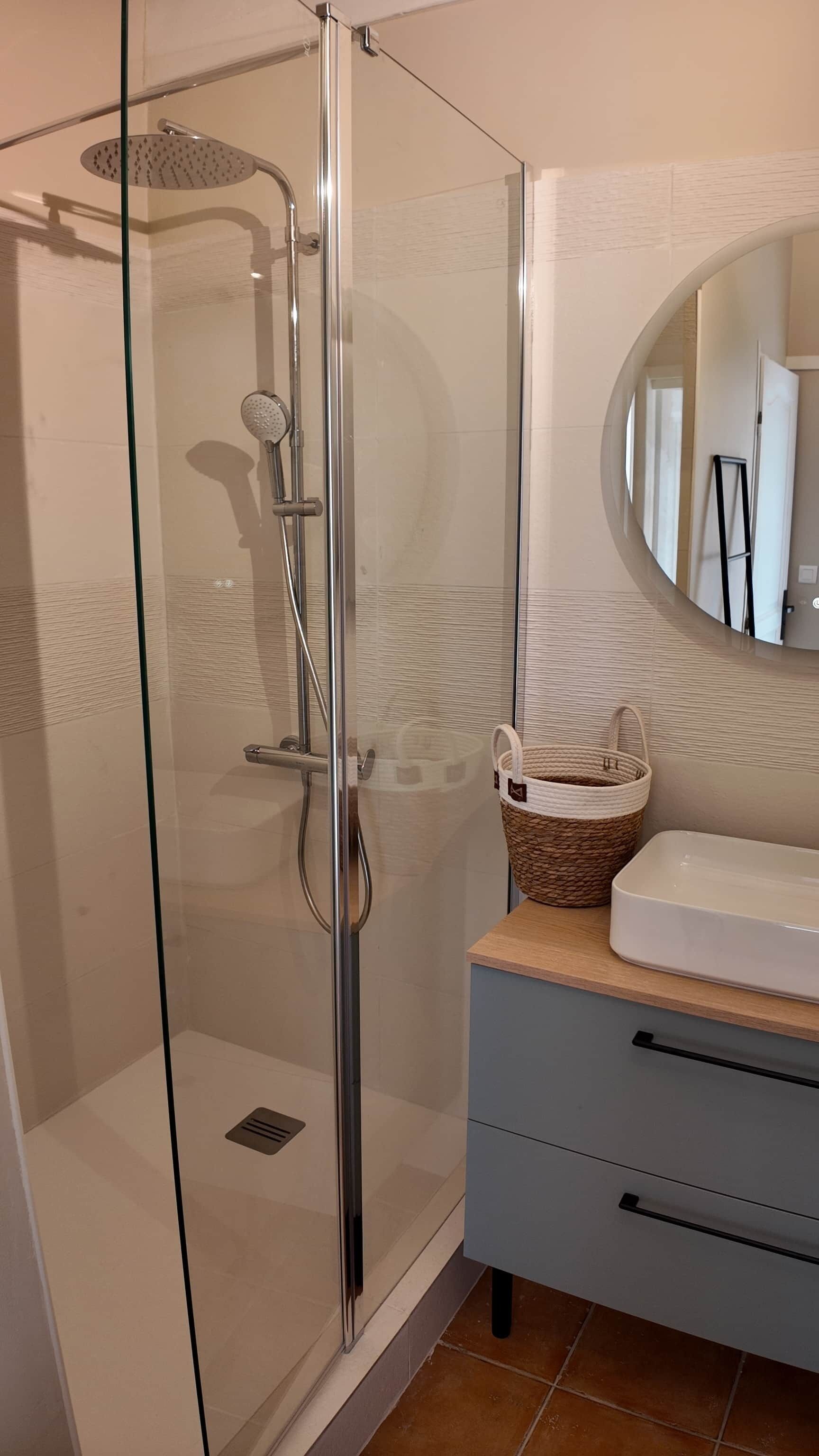 Ein modernes Badezimmer mit einer gläsernen Duschkabine, einem Waschbecken mit einem gewebten Korb und einem Spiegel.