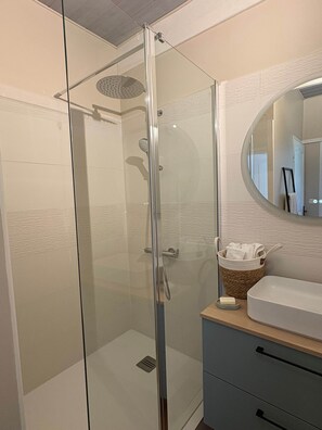 A glass-enclosed shower with a handheld showerhead, a wooden vanity with a sink, and a mirror with a round frame. - le Pitchounet, gite for 2 _ Lacets Ventoux (Beaumont-du-Ventoux)