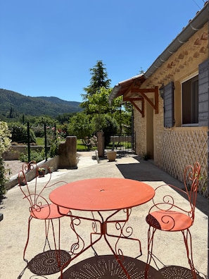A patio with a round table and chairs, a stone wall, and a view of a mountain. - le Pitchounet, gite for 2 _ Lacets Ventoux (Beaumont-du-Ventoux)