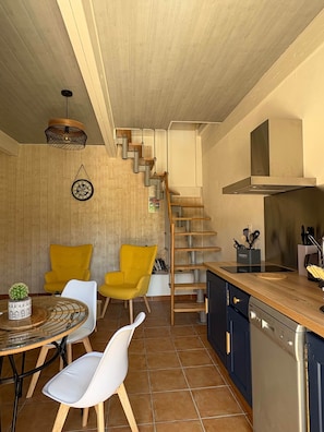 A modern kitchen with a wooden staircase, a dining area with yellow chairs, and a kitchen island. - le Pitchounet, gite for 2 _ Lacets Ventoux (Beaumont-du-Ventoux)