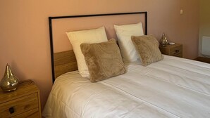 A bedroom with a bed, pillows, a nightstand, a lamp, and a framed artwork on the wall.