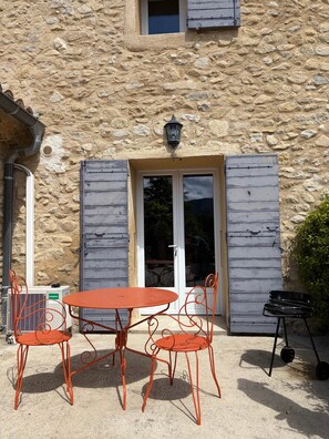 A stone building with a door, a window, and a table with chairs outside.