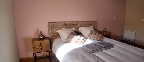 A bedroom with a wooden nightstand, a bed with white bedding, and a decorative vase on the nightstand.