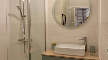 Un baño con cabina de ducha de vidrio, un espejo redondo, un lavabo con encimera de madera y una cesta.