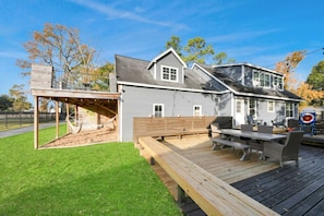 A house with a deck, a covered patio, and a backyard with a hammock. - Mossy Oaks Main House w/ Pool & Outdoor Games (Spring)