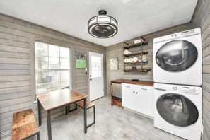 A laundry room with a washing machine, dryer, wooden floor, and a table with chairs. - Mossy Oaks Main House w/ Pool & Outdoor Games (Spring)