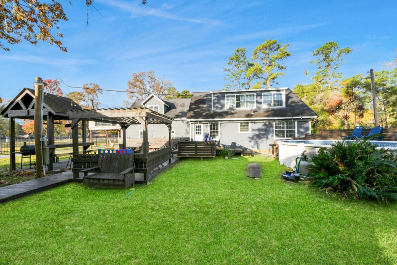 A house with a covered patio, a swimming pool, and a well-maintained lawn.