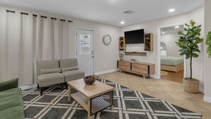 Ein Wohnzimmer mit Sofa, Couchtisch, Wand-Fernseher, einer kleinen Kommode und einem Blumentopf.