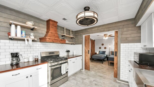 Una cocina moderna con armarios blancos, una estufa de acero inoxidable y techo de madera.