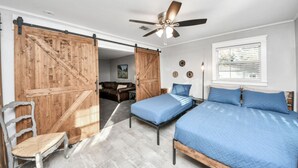Un dormitorio con dos camas, ventilador de techo, puerta corrediza estilo granero y una ventana con persianas.