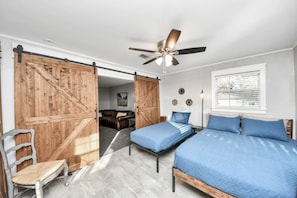 Un dormitorio con dos camas, ventilador de techo, puerta corrediza estilo granero y una ventana con persianas.