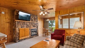 L’intérieur chaleureux d’un chalet avec une cheminée en pierre, un plafond en bois et un téléviseur fixé au mur.