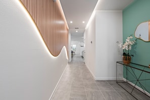 Ein moderner Flur mit einer Wand in Holzoptik, einer Wand in Türkis und einem Metall-Konsolentisch mit einem Blumentopf.