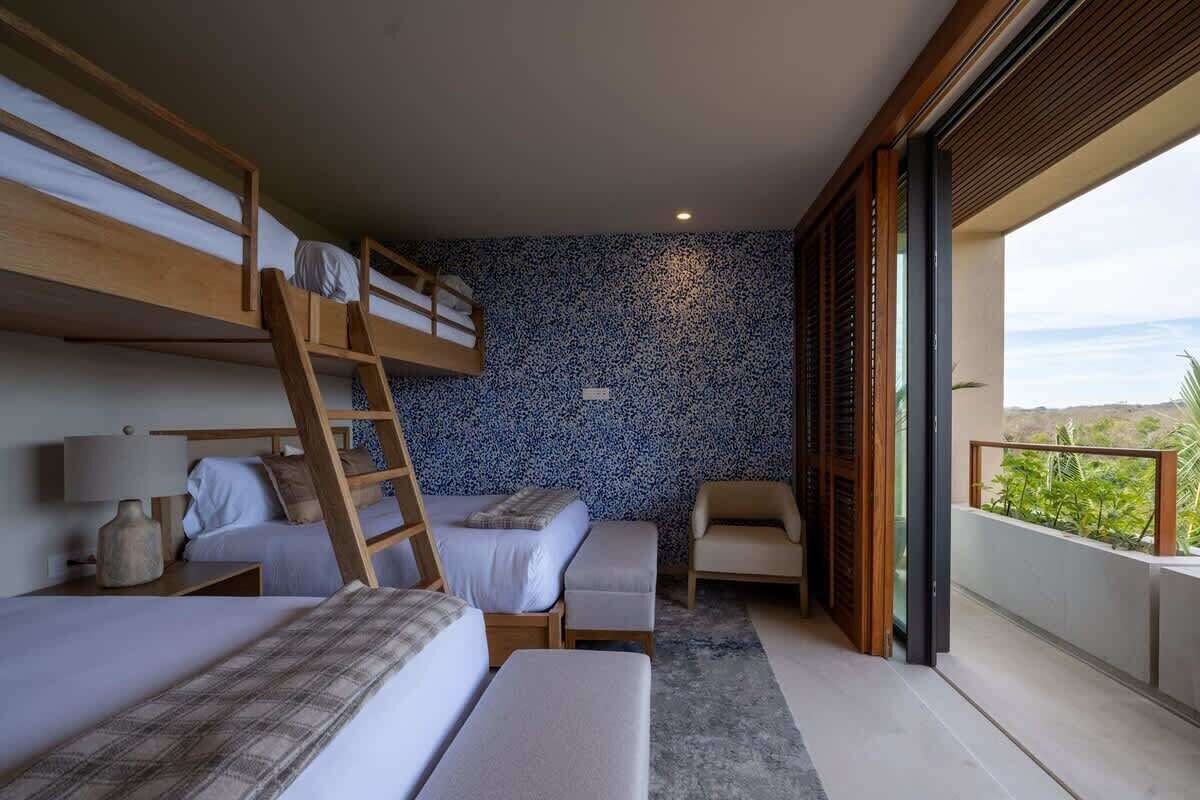 A room with bunk beds, a desk, a chair, and a balcony with a view.