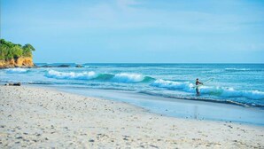 Une plage avec un ciel dégagé, des vagues et une personne tenant une planche de surf.