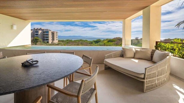 Un espace extérieur moderne, aménagé pour se détendre, avec une table ronde et des chaises, un canapé et une vue sur un bâtiment et la verdure.