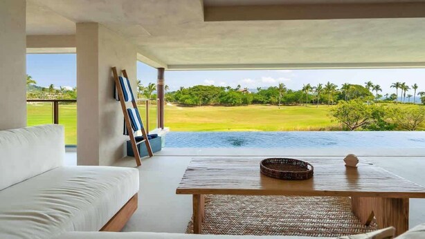 Una stanza moderna con un divano bianco, un tavolo di legno e vista su un campo da golf e un corpo d'acqua.