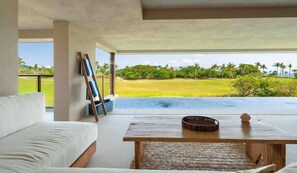 A modern room with a white sofa, a wooden table, and a view of a golf course and water body. - Amazing Golf Views+2 Golf Carts in Punta Mita (Punta Mita)