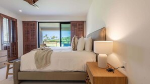 Camera da letto moderna con un letto grande, un comodino con una lampada e vista su un balcone con palme.