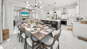 Una cocina moderna con armarios blancos, una isla grande y una zona de comedor con una mesa y sillas de madera.