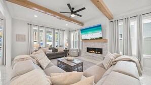 A spacious living room with a fireplace, large windows, and a ceiling fan. - 5BR 30A Oasis •Private Pool + Hot Tub • Pet Friendly • Bike to Beach • Golf Cart (Santa Rosa Beach)