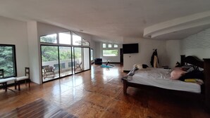 A spacious bedroom with a large bed, a TV mounted on the wall, and a sliding glass door leading to a balcony. - Escape to Your Private Costa Rican Jungle Retreat (Atenas)