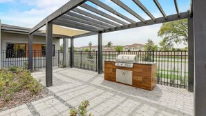 An outdoor patio area with a grill station and a pergola structure. - 3BR Home Near Disney w/ Office & Fun Corner (Kissimmee)