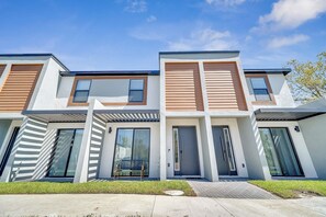A modern multi-story residential building with large windows, a covered outdoor seating area, and a well-maintained lawn. - 3BR Home Near Disney w/ Office & Fun Corner (Kissimmee)