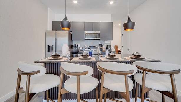 A modern kitchen with a central island, bar stools, and pendant lighting. - 3BR Home Near Disney w/ Office & Fun Corner (Kissimmee)