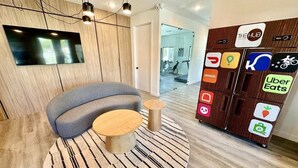 A modern waiting area with a grey sofa, two wooden side tables, a large round rug, and a wall-mounted TV. - 3BR Home Near Disney w/ Office & Fun Corner (Kissimmee)