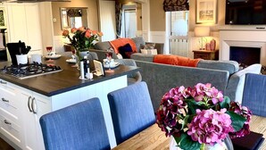 Ein modernes Wohnzimmer mit grauem Sofa, blauen Sesseln, einem Esstisch und einer Küchenzeile mit Gasherd.