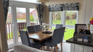 Ein gemütliches Wohnzimmer mit einem Holzesstisch, grauen Sofas und Blick ins Freie durch große Fenster.