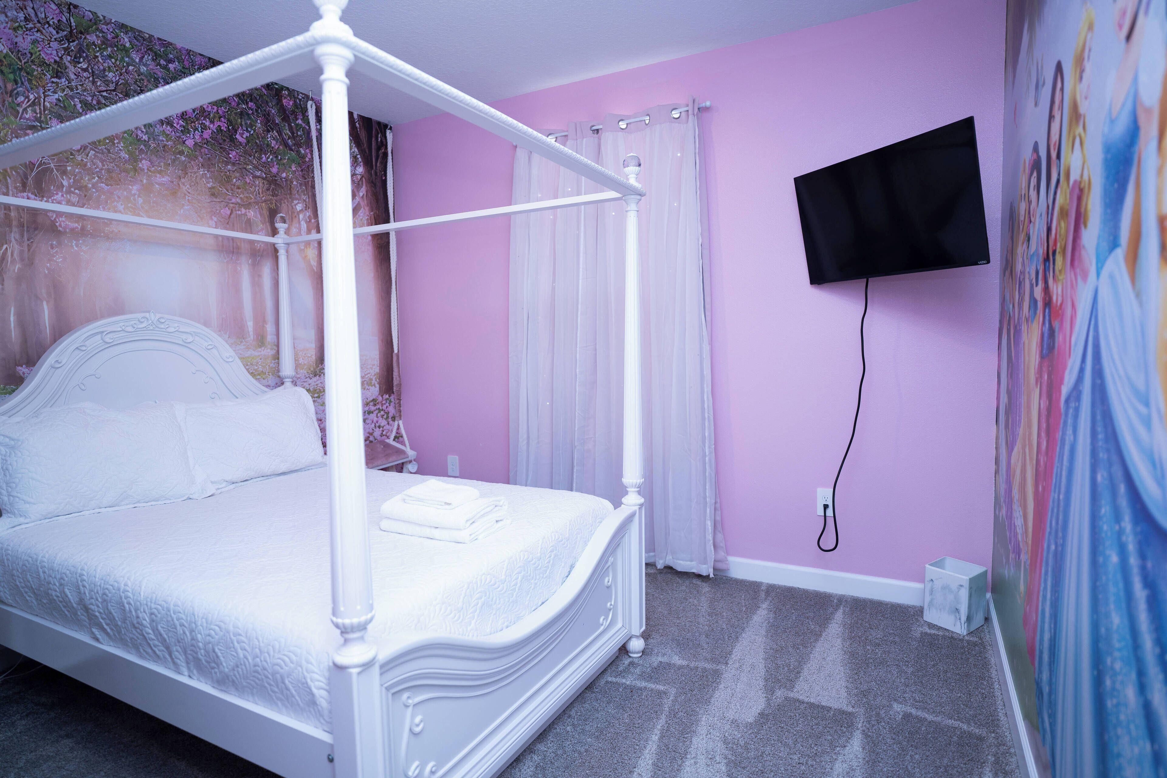A four-poster bed with a canopy, a flat-screen TV mounted on the wall, and a floral mural on the wall.