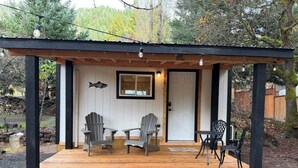 Een houten terras met twee Adirondack-stoelen, een tafel, een deur en een decoratie van een vis.