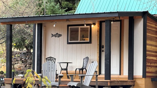 Een chalet met een veranda, twee Adirondack-stoelen, een kleine tafel en een stenen muur op de achtergrond.