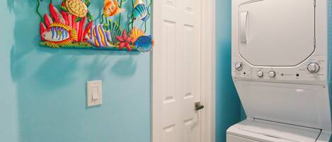 A laundry room with a white washer and dryer, a door, and a colorful fish mural on the wall.