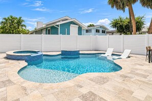 Una piscina con un design curvo, circondata da un recinto bianco, con una casa sullo sfondo.