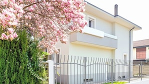 Een modern huis met twee verdiepingen, een witte gevel, een metalen hek en een boom met roze bloemen.