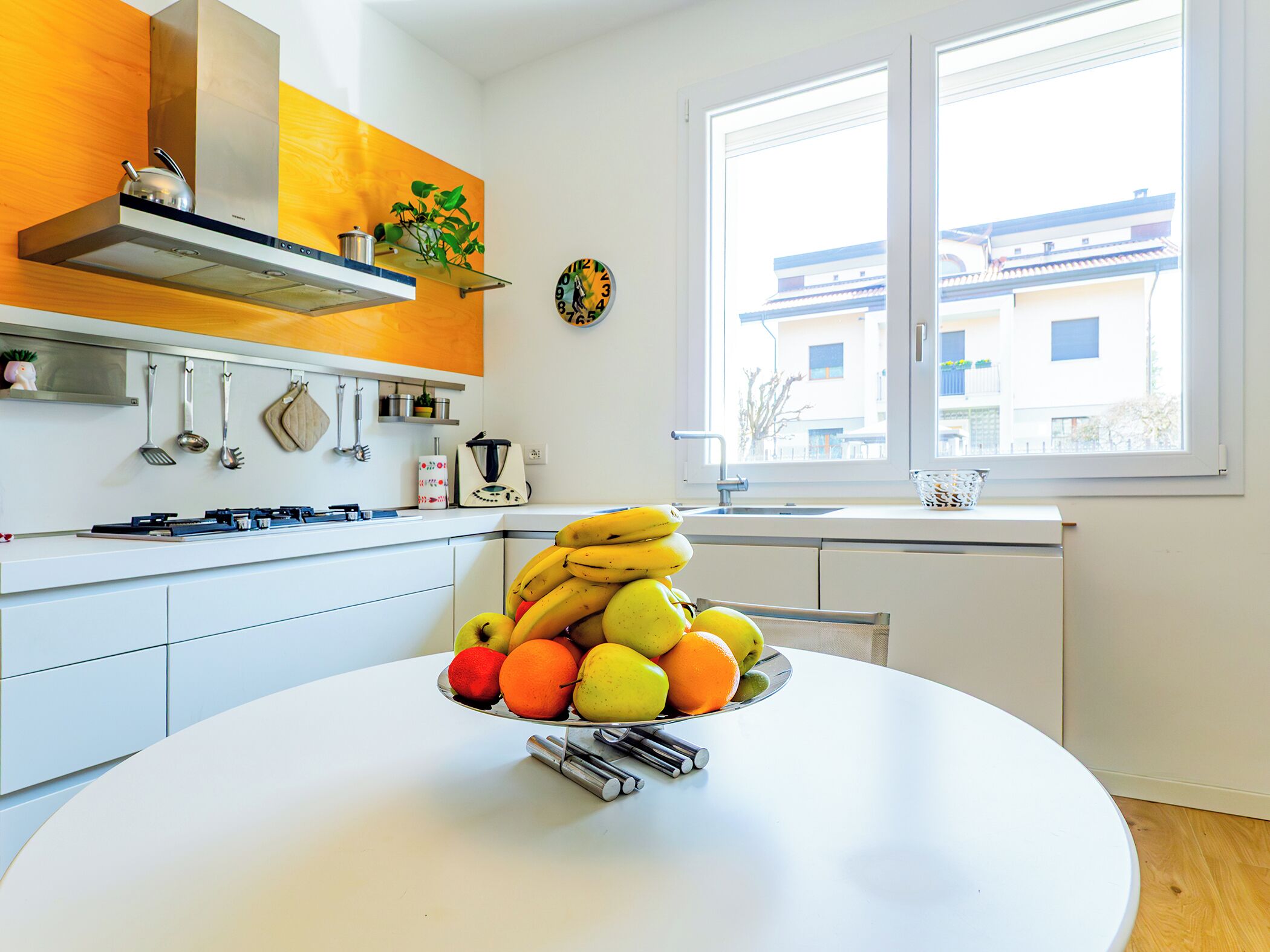 Une cuisine moderne avec des armoires blanches, une hotte de cuisinière en acier inoxydable et une fenêtre donnant sur les bâtiments environnants.