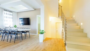 Een moderne woonkamer met een eetgedeelte, een trap en een flatscreen televisie aan de wand.
