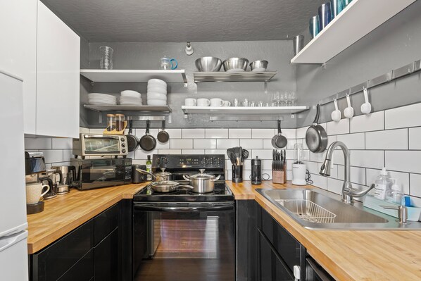 Une cuisine moderne avec des appareils électroménagers noirs, des plans de travail en bois et un dosseret de carrelage blanc.