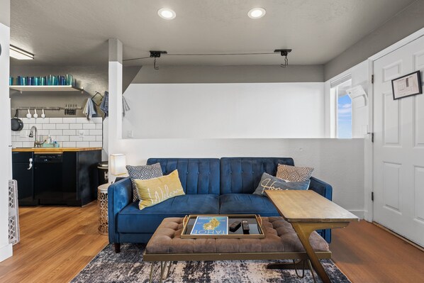 A modern living room with a blue sofa, a coffee table, and a kitchen area in the background. - Valley View Condo - Stay 3 Nights, Get 4th Free (Stateline)