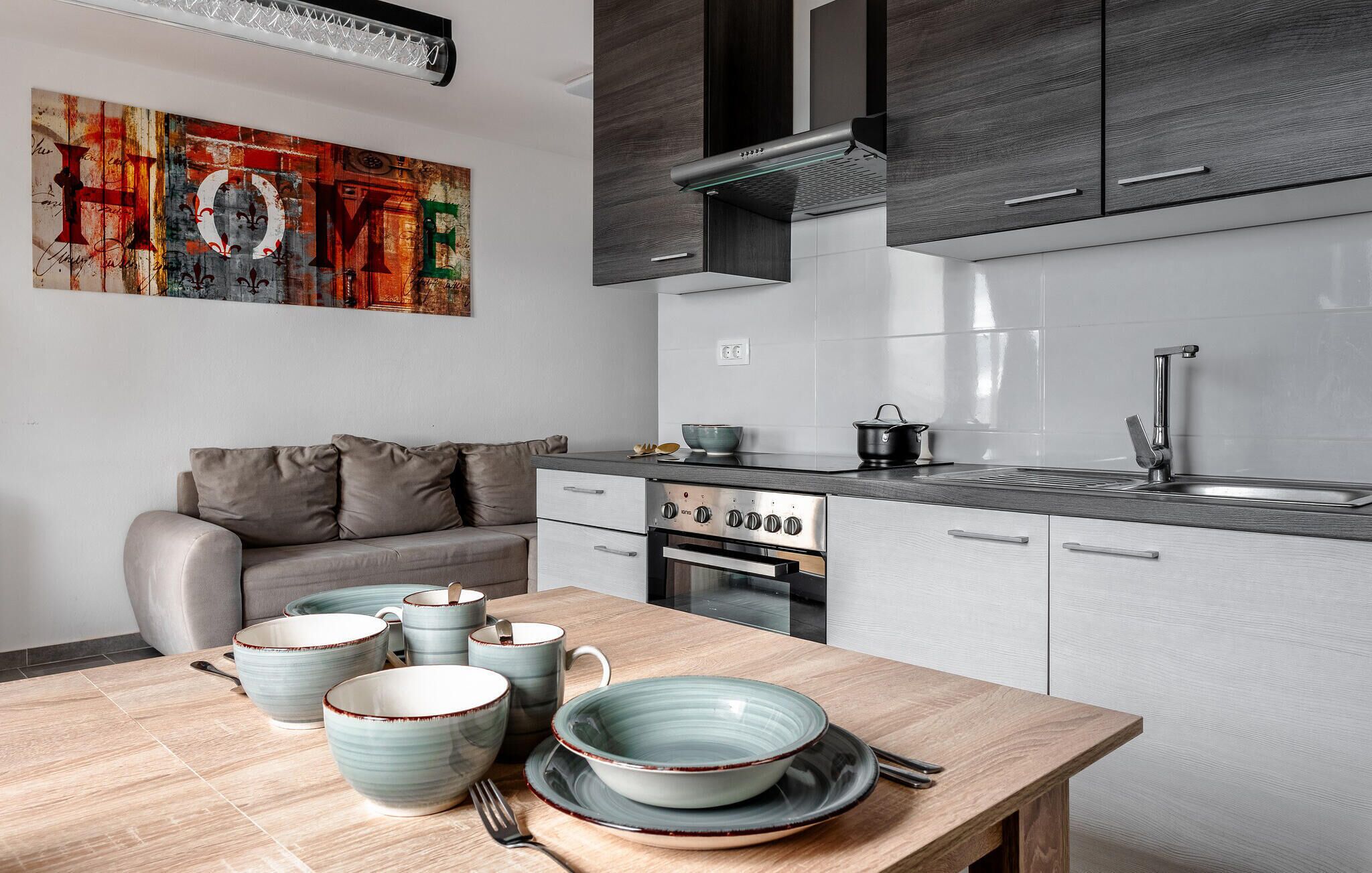 Een moderne keuken met grijze kastjes, een inbouwoven en een RVS-gootsteen.