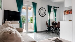 A modern living room with a sofa, a flat-screen TV, a dining area with chairs, a table, and a clock on the wall. - Luxurious apartment in Vir with house sea view (Vir)