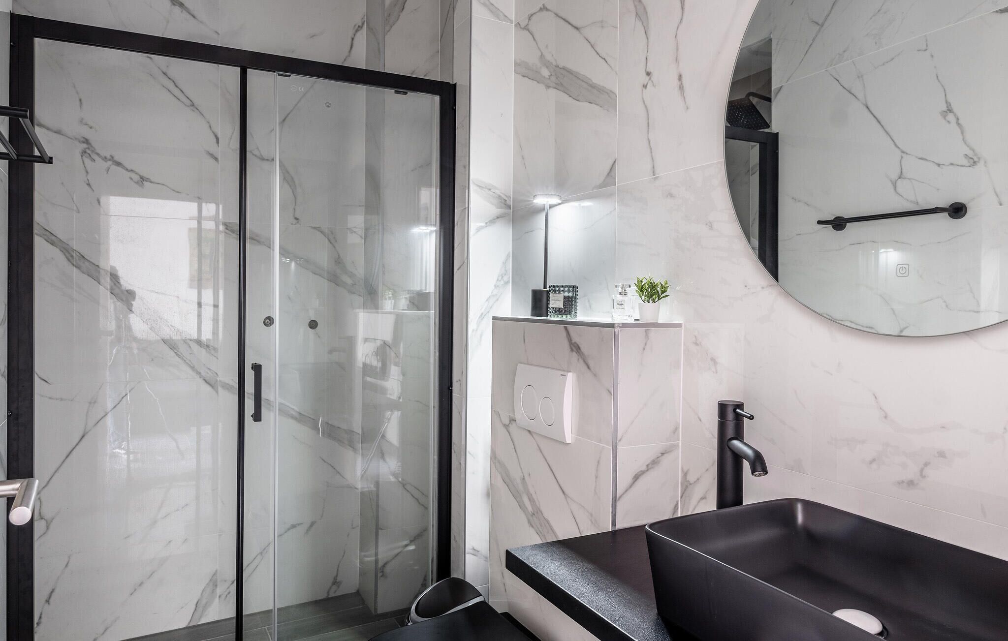 A modern bathroom with a glass shower enclosure, a black freestanding sink, and a marble-tiled wall.