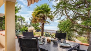 Un espace de restauration en plein air avec une table dressée pour deux personnes, entourée de chaises, offrant une vue panoramique sur la mer et une végétation luxuriante.
