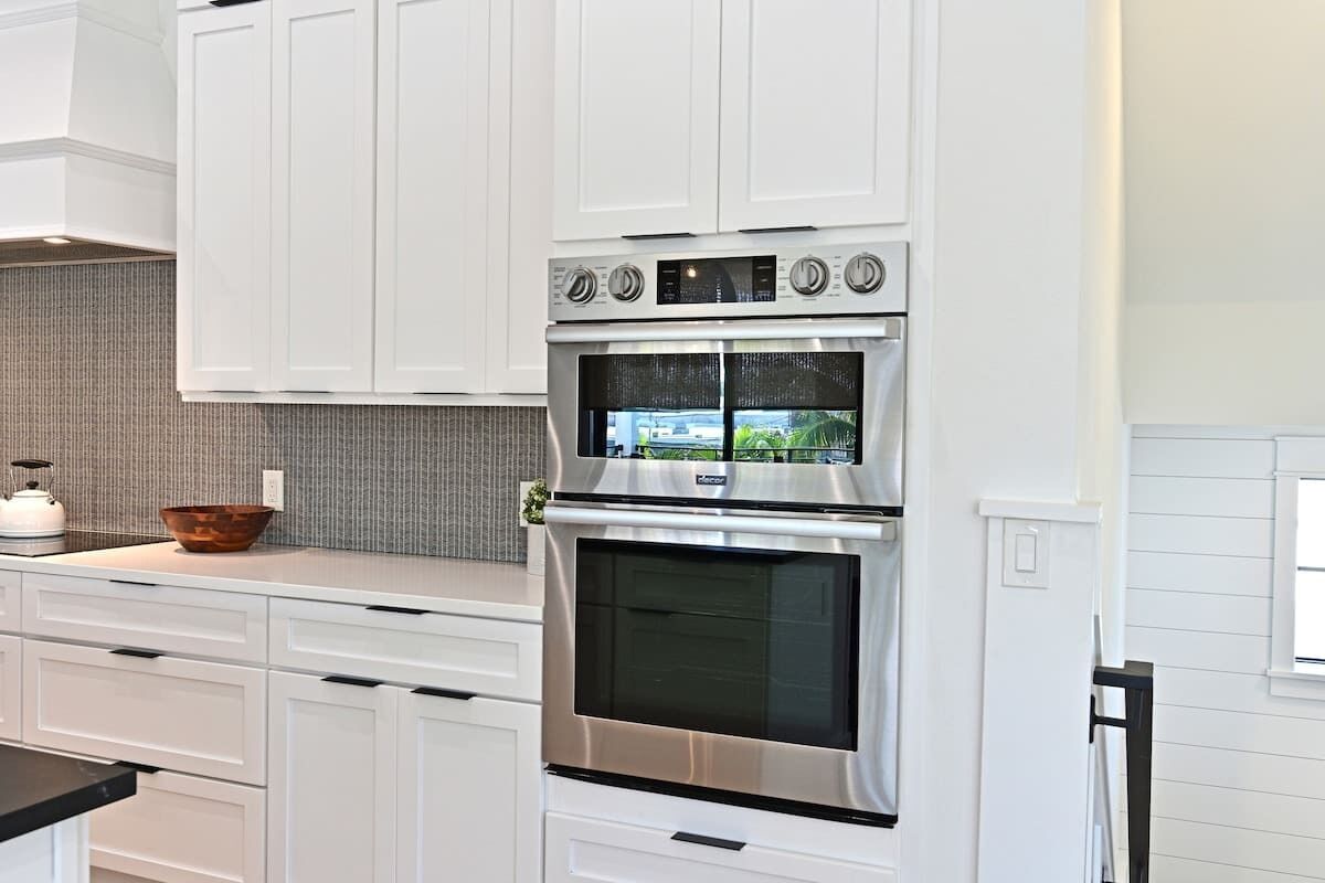 A modern kitchen with white cabinetry, a stainless steel oven, and a large window above the oven.