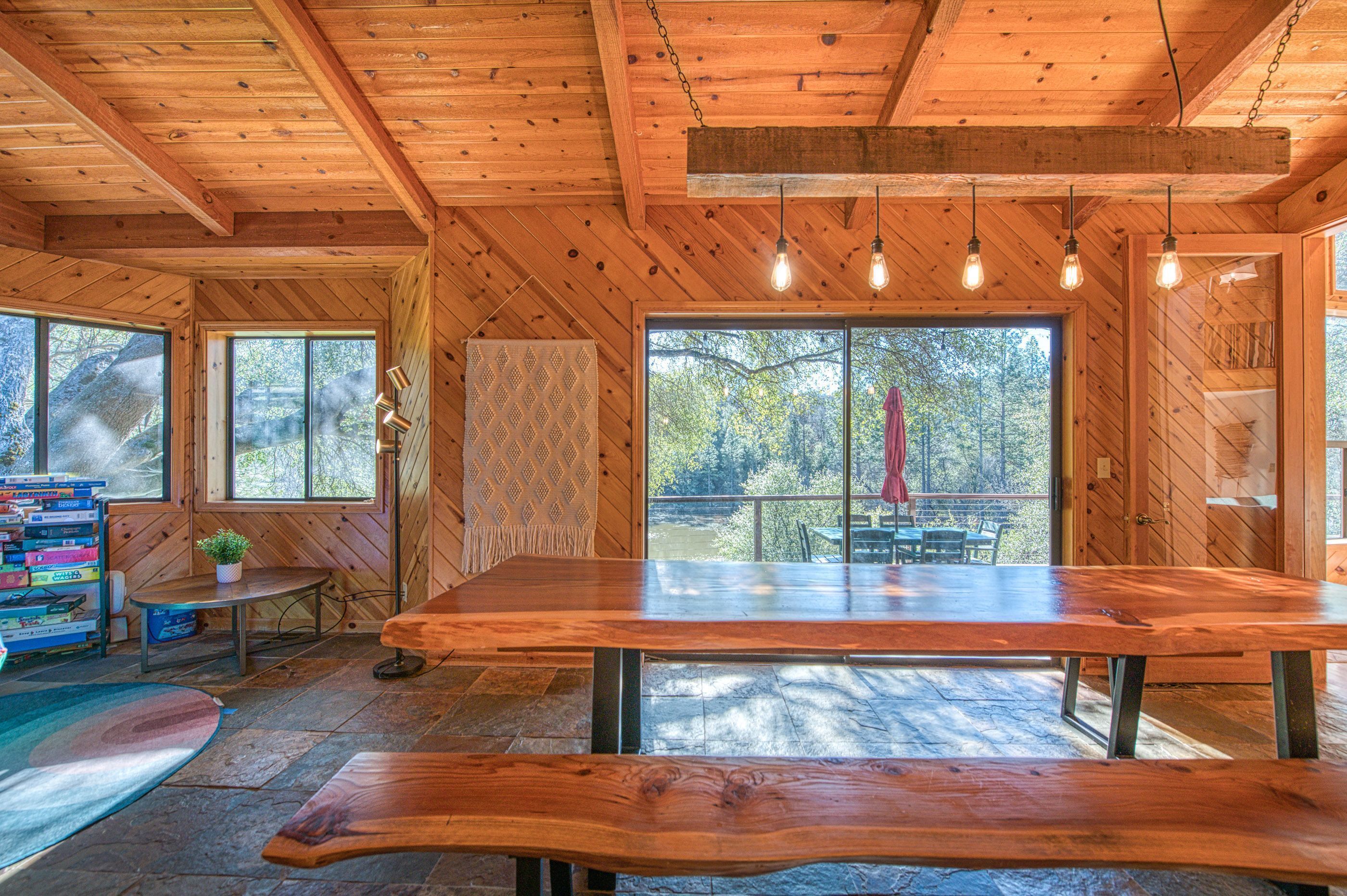 Ein Holzinterieur mit einem großen Esstisch, mehreren Fenstern und Blick ins Freie.